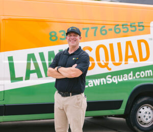 A Man standing with his arms crossed in front of a lawn squad van